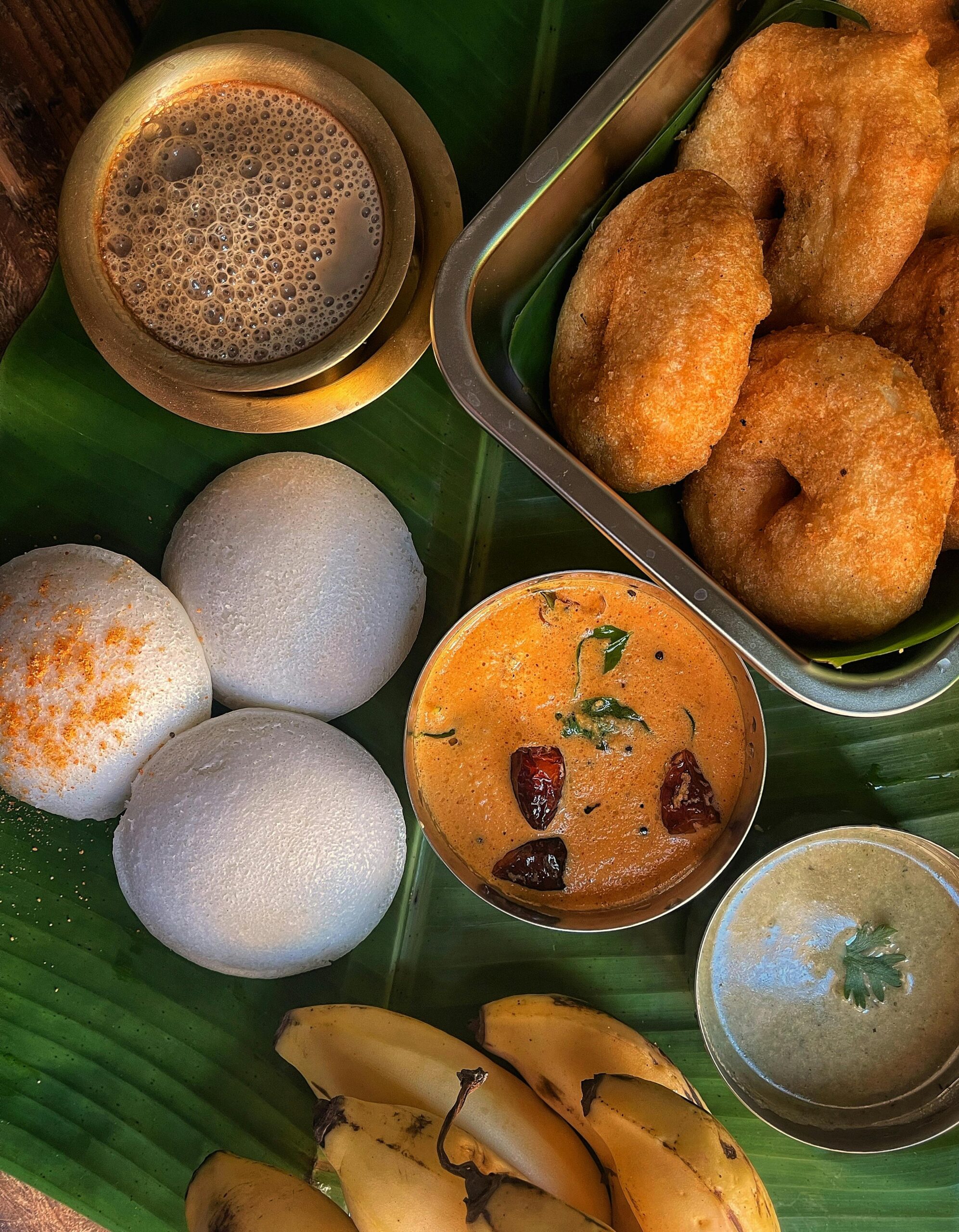 Contact Delicious South Indian breakfast with idli, vada, chutney, and coffee on banana leaf.